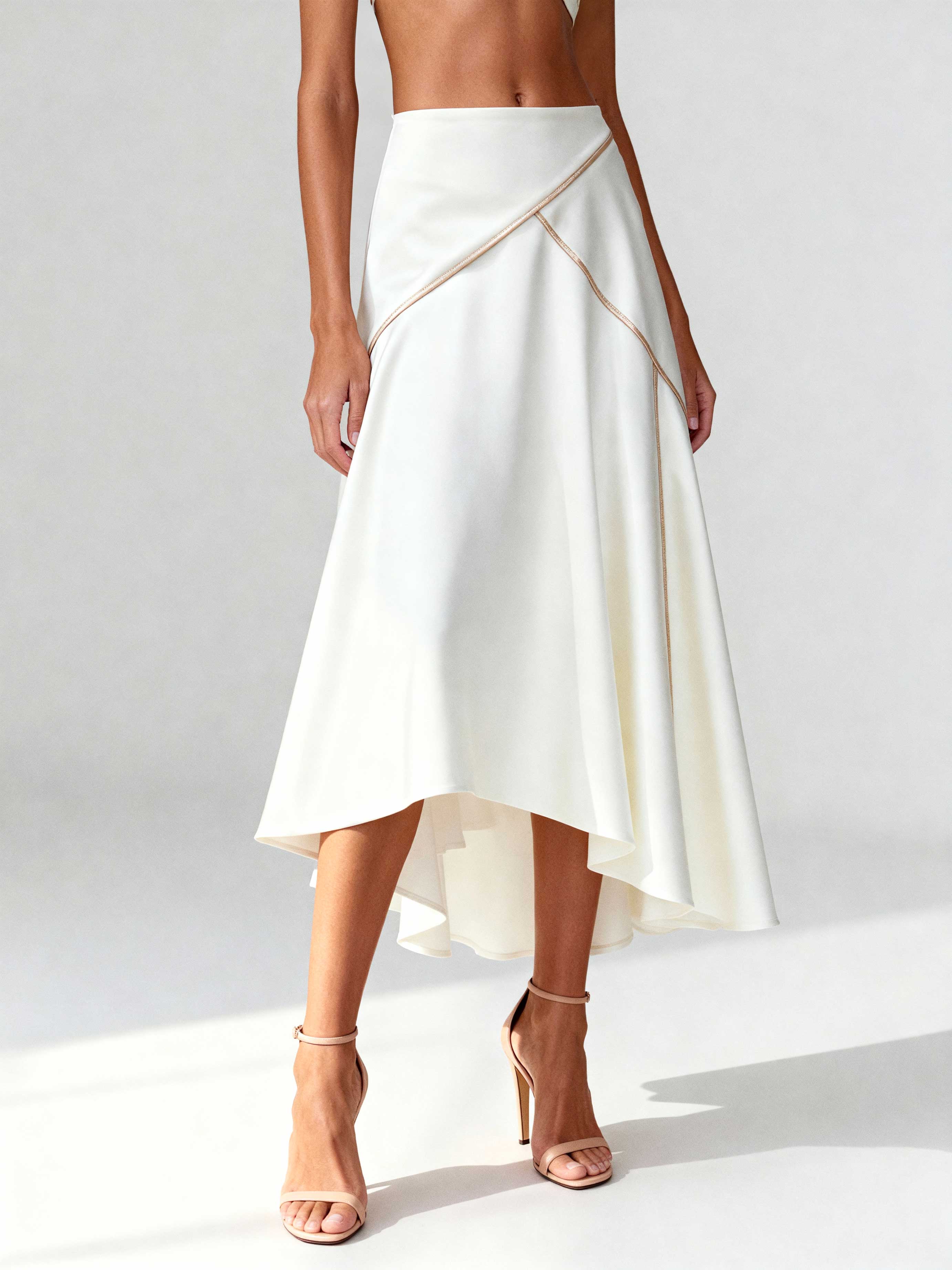 Close-up of asymmetrical white skirt with contrast piping and clean draping, styled with nude heels.