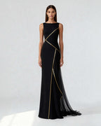 Long black evening gown with golden satin piping and sheer chiffon panel, worn by model standing in front view.