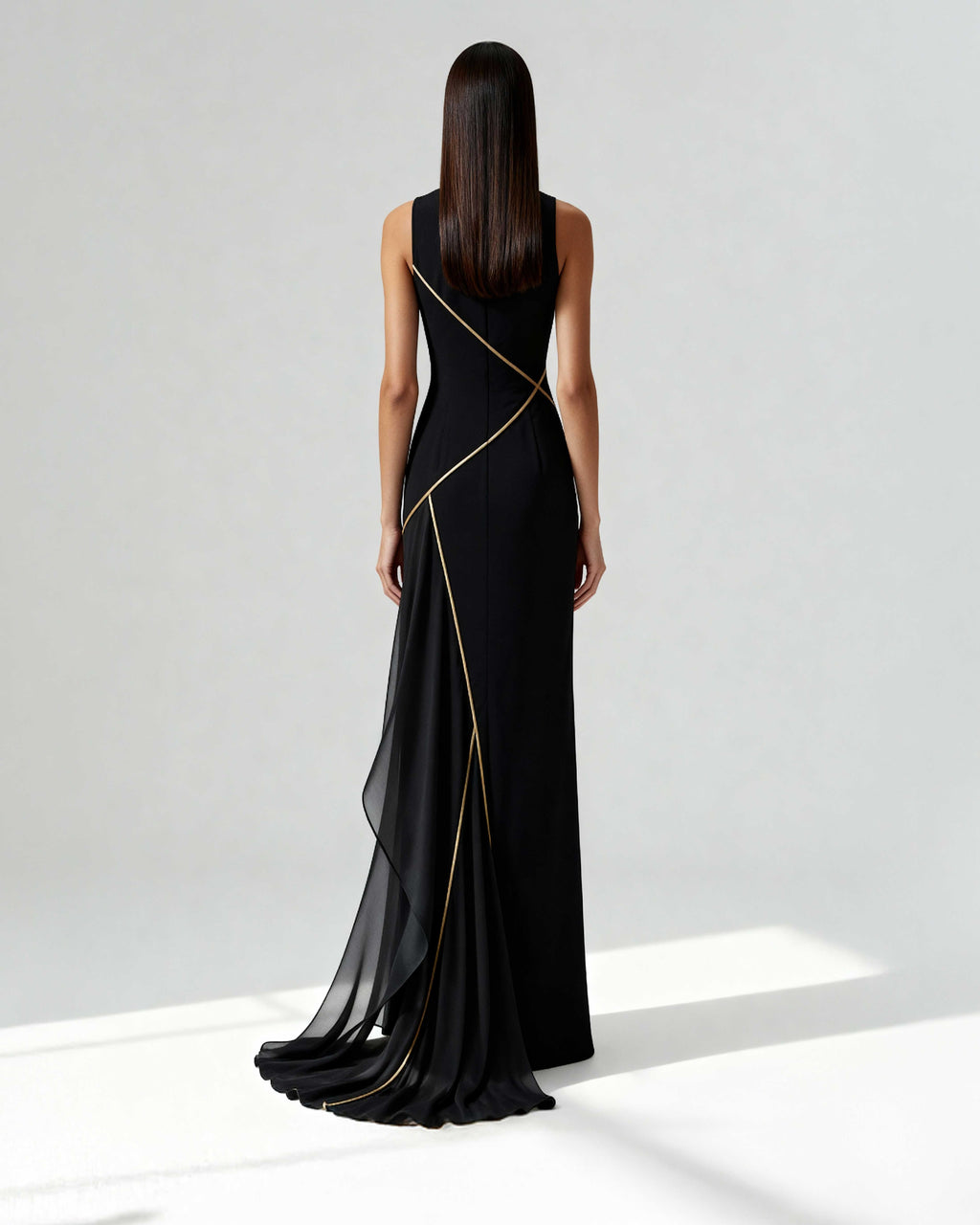 Back view of a long black gown with asymmetrical golden piping and sheer chiffon train, worn by model.