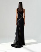Back view of a long black gown with asymmetrical golden piping and sheer chiffon train, worn by model.