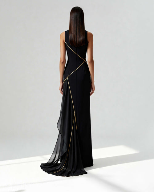 Back view of a long black gown with asymmetrical golden piping and sheer chiffon train, worn by model.