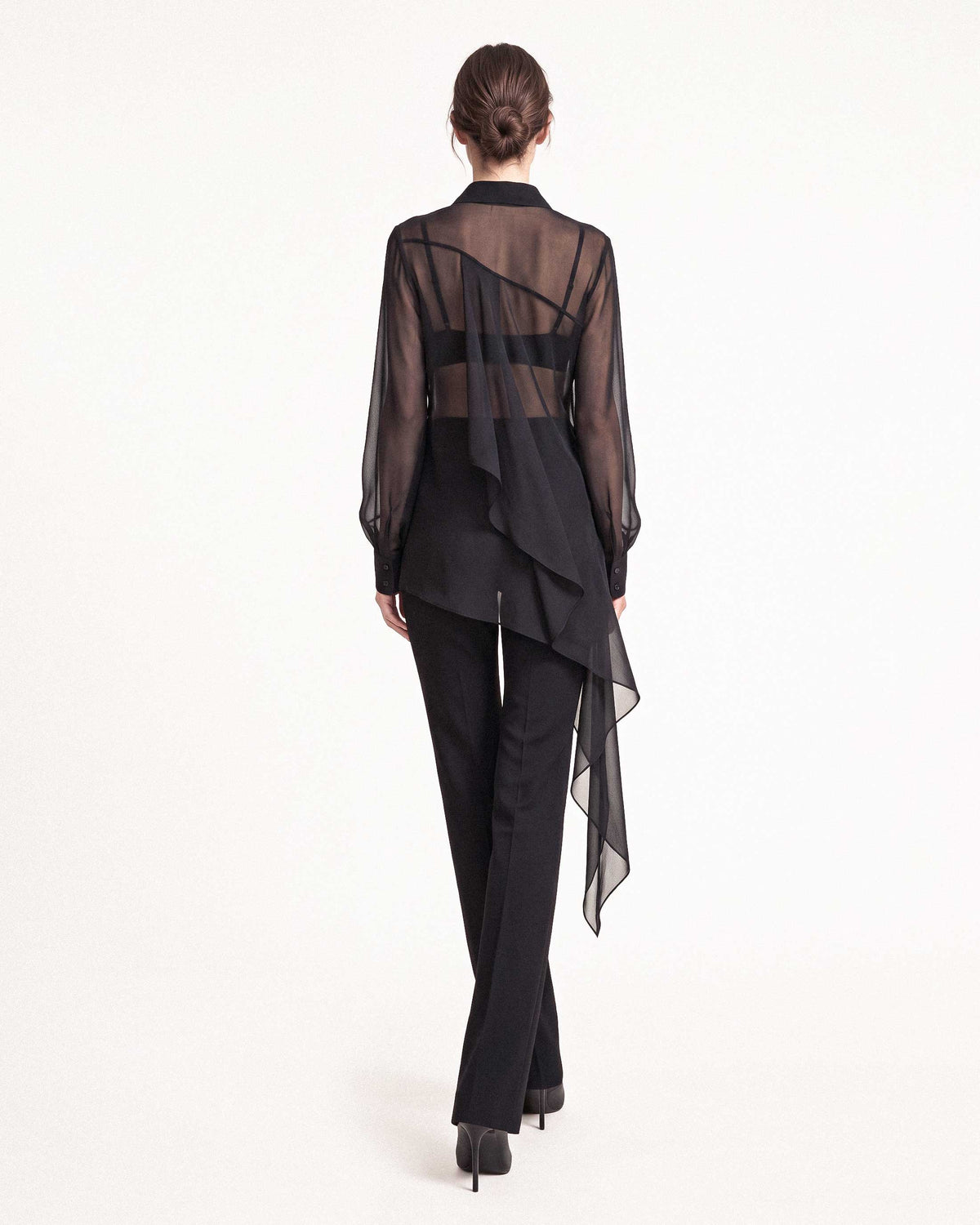 Back view of the black sheer silk chiffon shirt showing the transparent silk chiffon and asymmetric draped hem with black tailored crepe trousers by A|LOUD
