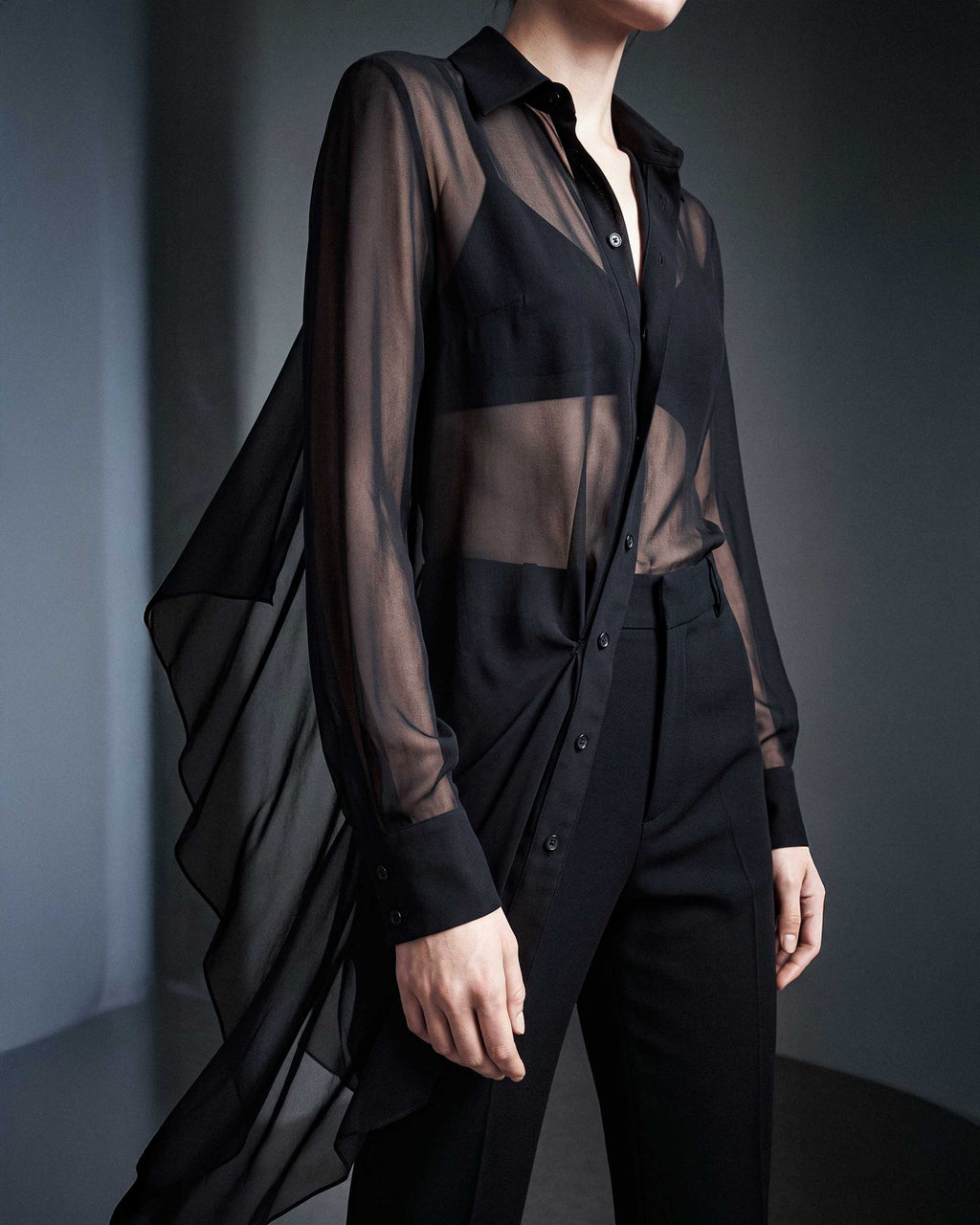 Side detail of the black sheer silk chiffon shirt showing the transparent fabric, long sleeves and asymmetric draped hem by A|LOUD