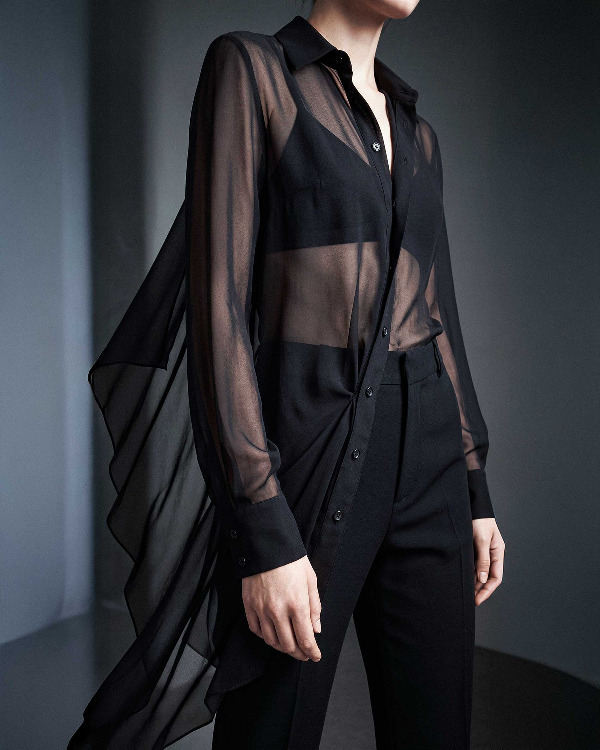 Side detail of the black sheer silk chiffon shirt showing the transparent fabric, long sleeves and asymmetric draped hem by A|LOUD