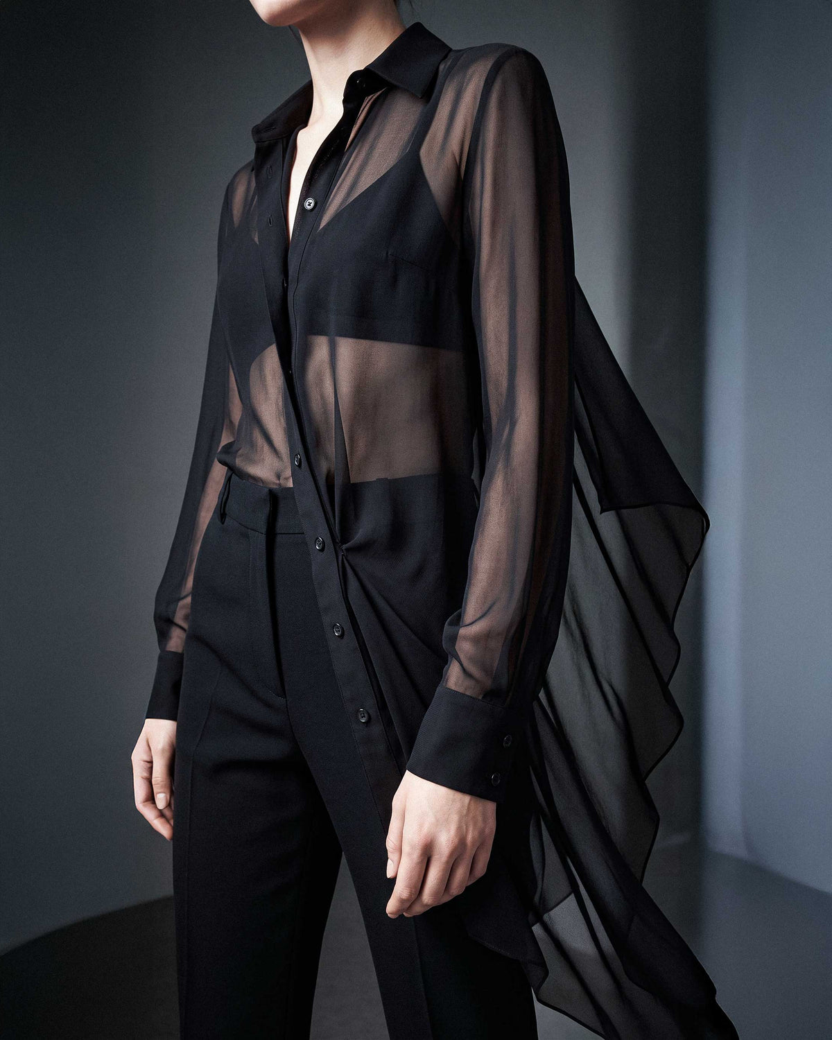 Side detail of the black sheer silk chiffon shirt showing the sheer silk chiffon drape and tailored black trousers by A|LOUD