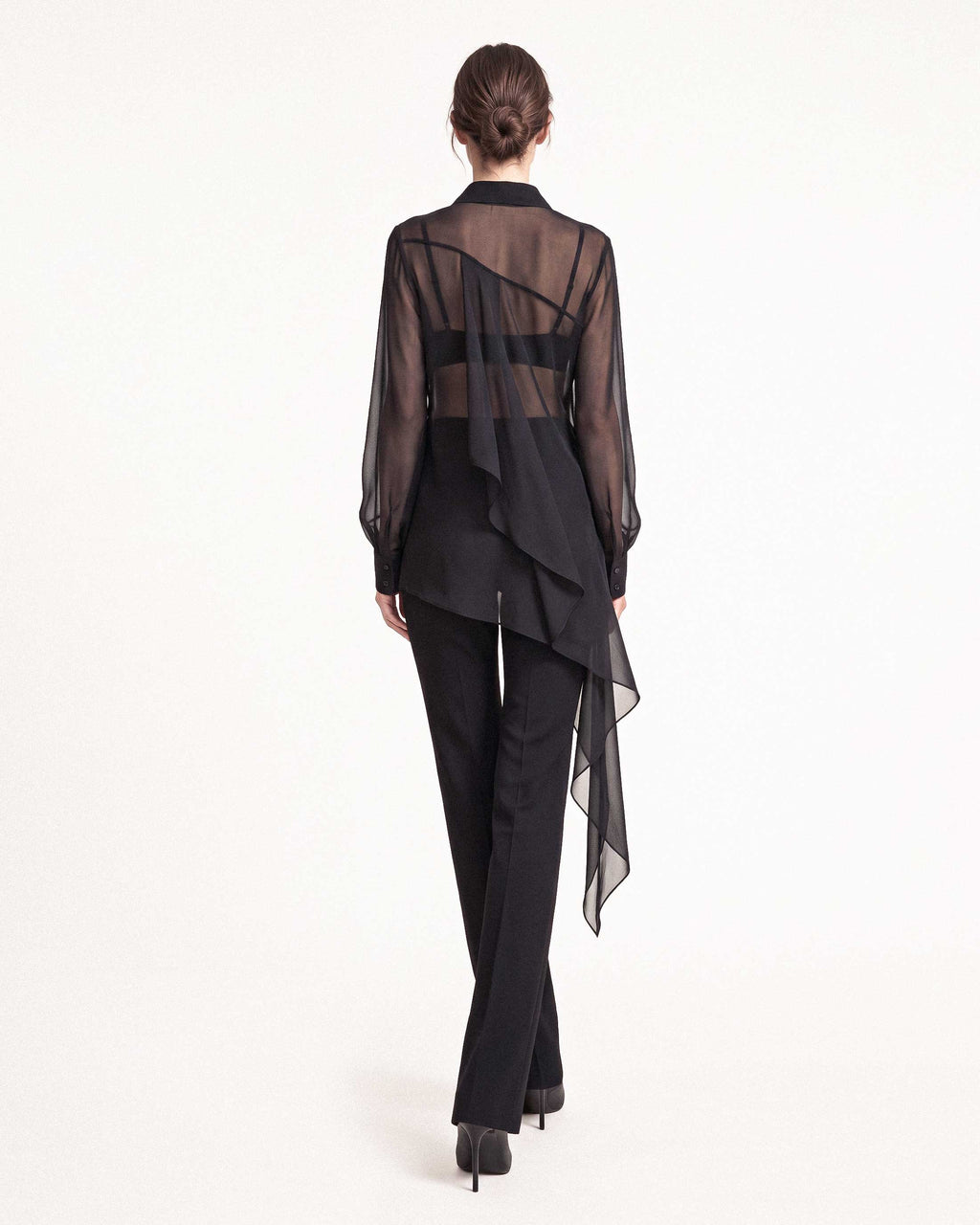 Back view of the black sheer silk chiffon shirt showing the transparent silk chiffon and asymmetric draped hem with black tailored crepe trousers by A|LOUD