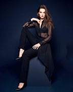 Model seated wearing a black sheer silk chiffon shirt with black tailored crepe trousers in an editorial studio image by A|LOUD