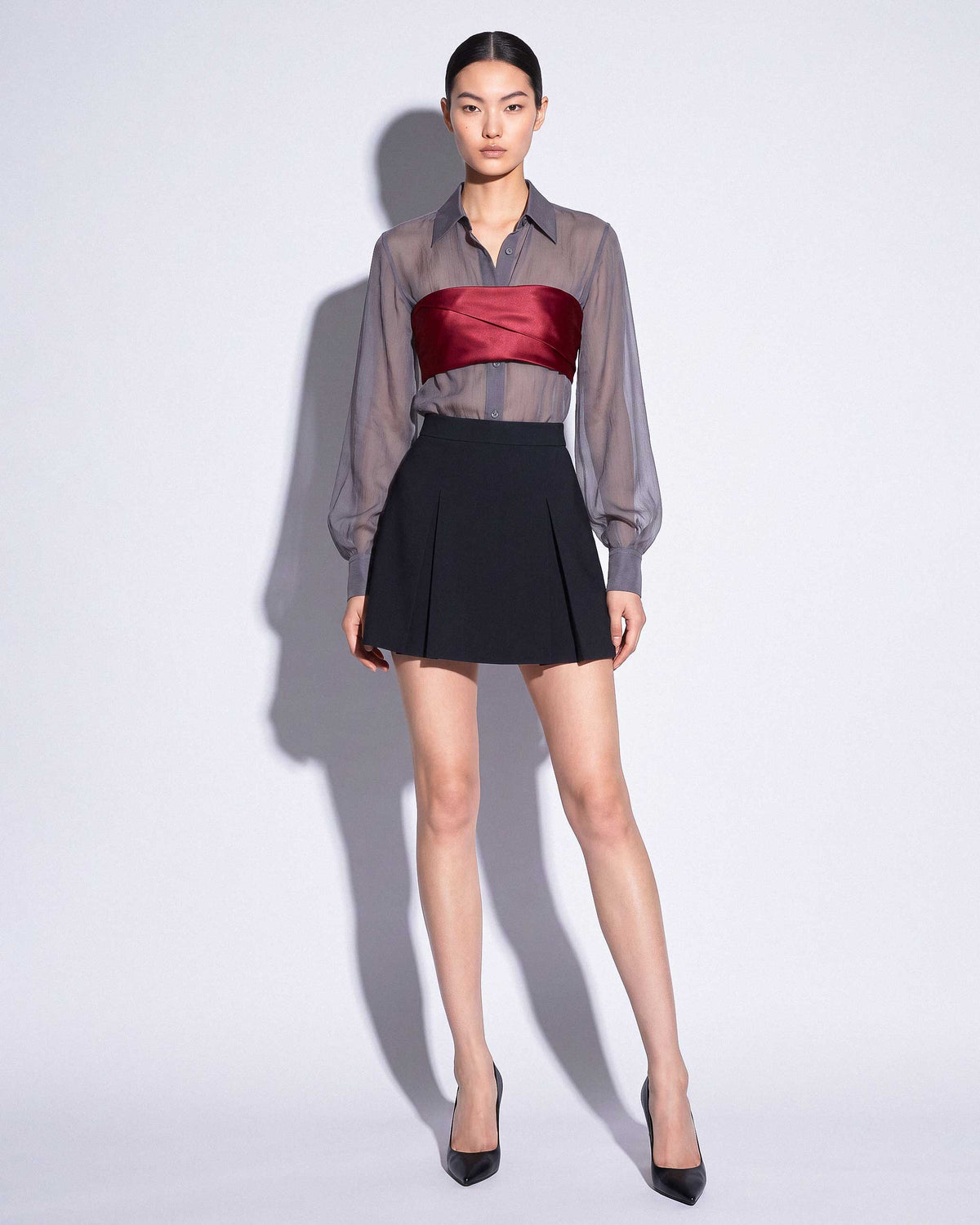 Full front look of the ÉLYR burgundy silk satin bandeau styled with a sheer charcoal silk chiffon shirt and black mini skirt by A|LOUD