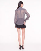 Three-quarter back view of the ÉLYR sheer charcoal silk chiffon shirt and black mini skirt by A|LOUD