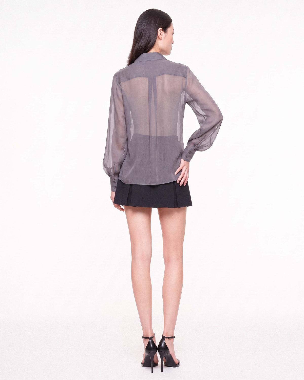 Three-quarter back view of the ÉLYR sheer charcoal silk chiffon shirt and black mini skirt by A|LOUD