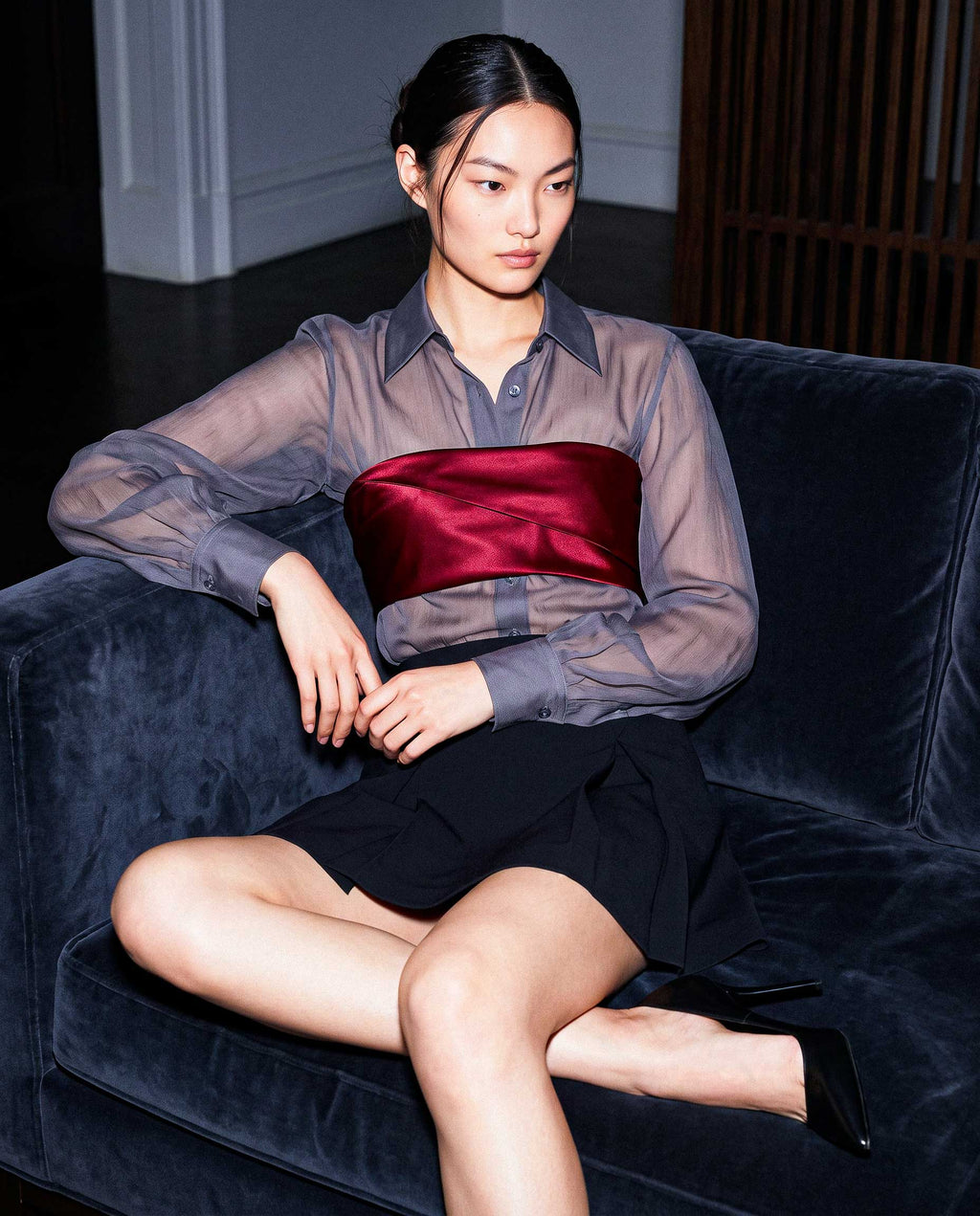 Model seated wearing the ÉLYR sheer charcoal silk chiffon shirt, burgundy silk satin bandeau and black mini skirt by A|LOUD