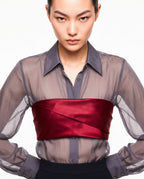 Close-up of the ÉLYR sheer charcoal silk chiffon shirt styled with a burgundy silk satin bandeau, showing the transparent texture, pointed collar and sculptural satin wrap by A|LOUD