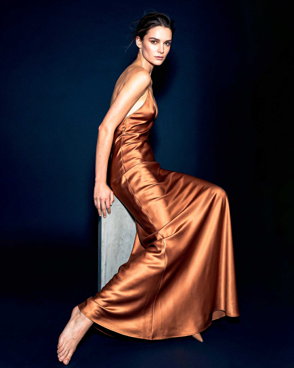 Editorial photograph of the SEREA copper satin slip dress showcasing fluid movement and elegant satin texture.