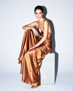 Full-length editorial view of the SEREA copper satin slip dress with sculptural bias-cut silhouette.