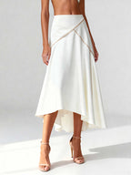Close-up of asymmetrical white skirt with contrast piping and clean draping, styled with nude heels.