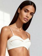 Model wearing structured white bustier top with curved neckline and satin piping, captured in soft natural light.