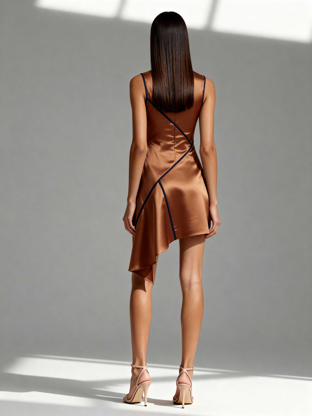 Model wearing copper satin mini dress with navy piping and draped back – back view