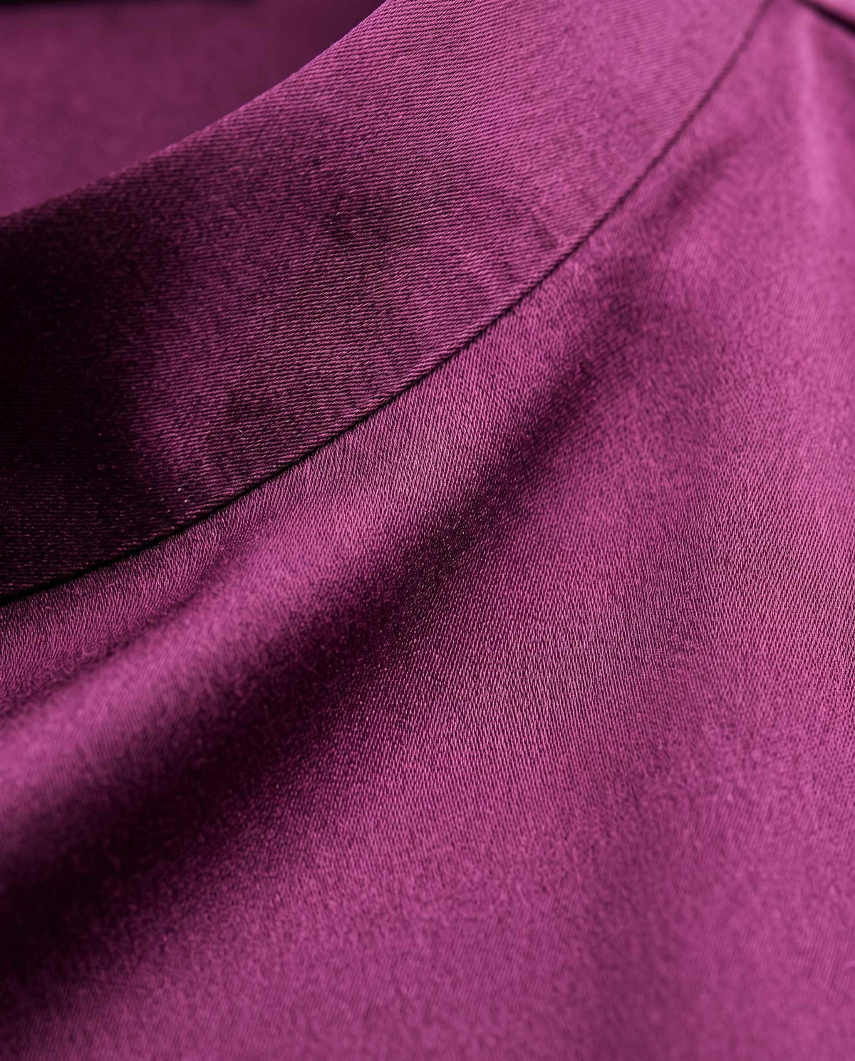 Close up of plum silk satin showing its sheen, fine texture and stitched seam.