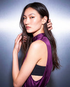 Side portrait of a model wearing the A|LOUD plum silk satin top with a high neckline and a deep side opening over a black bandeau.