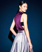 Three quarter back view of the plum silk satin top with open sides, paired with a silver grey pleated skirt.