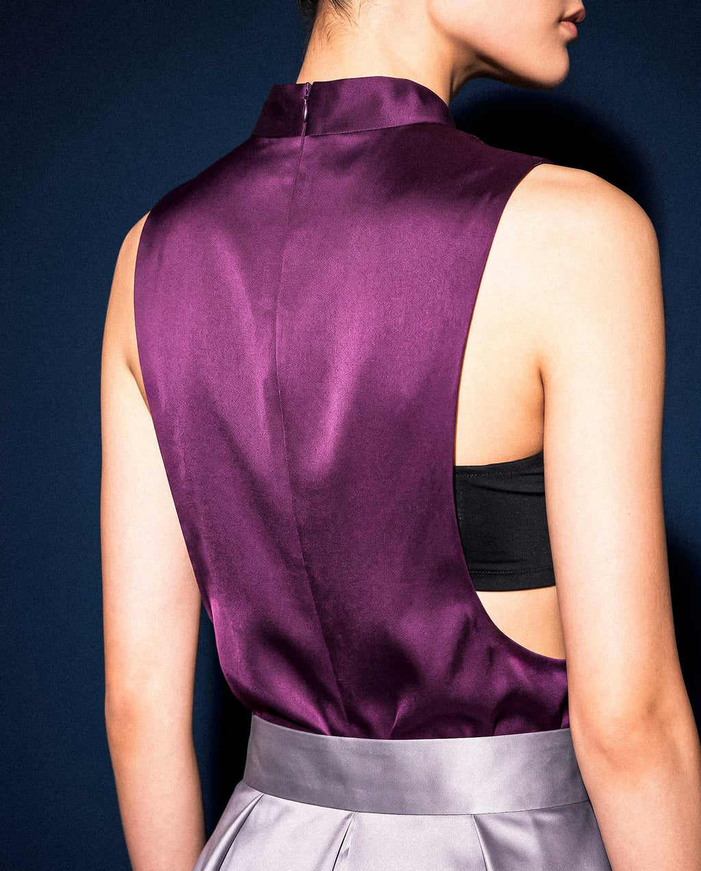 Back detail of the plum silk satin top showing the concealed neckline zip and deep side opening with a black bandeau underneath.