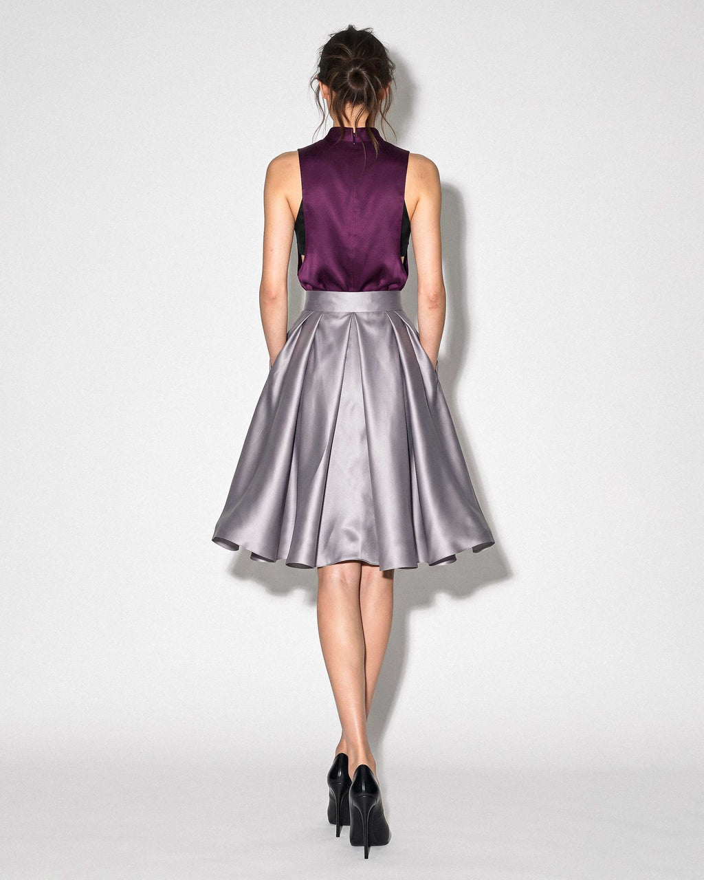 Full back view of the A|LOUD silver grey pleated silk satin skirt, styled with a plum top against a light grey background.