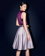 Three quarter back view of the silver grey pleated silk satin skirt with a defined waistband, styled with a plum open side top.