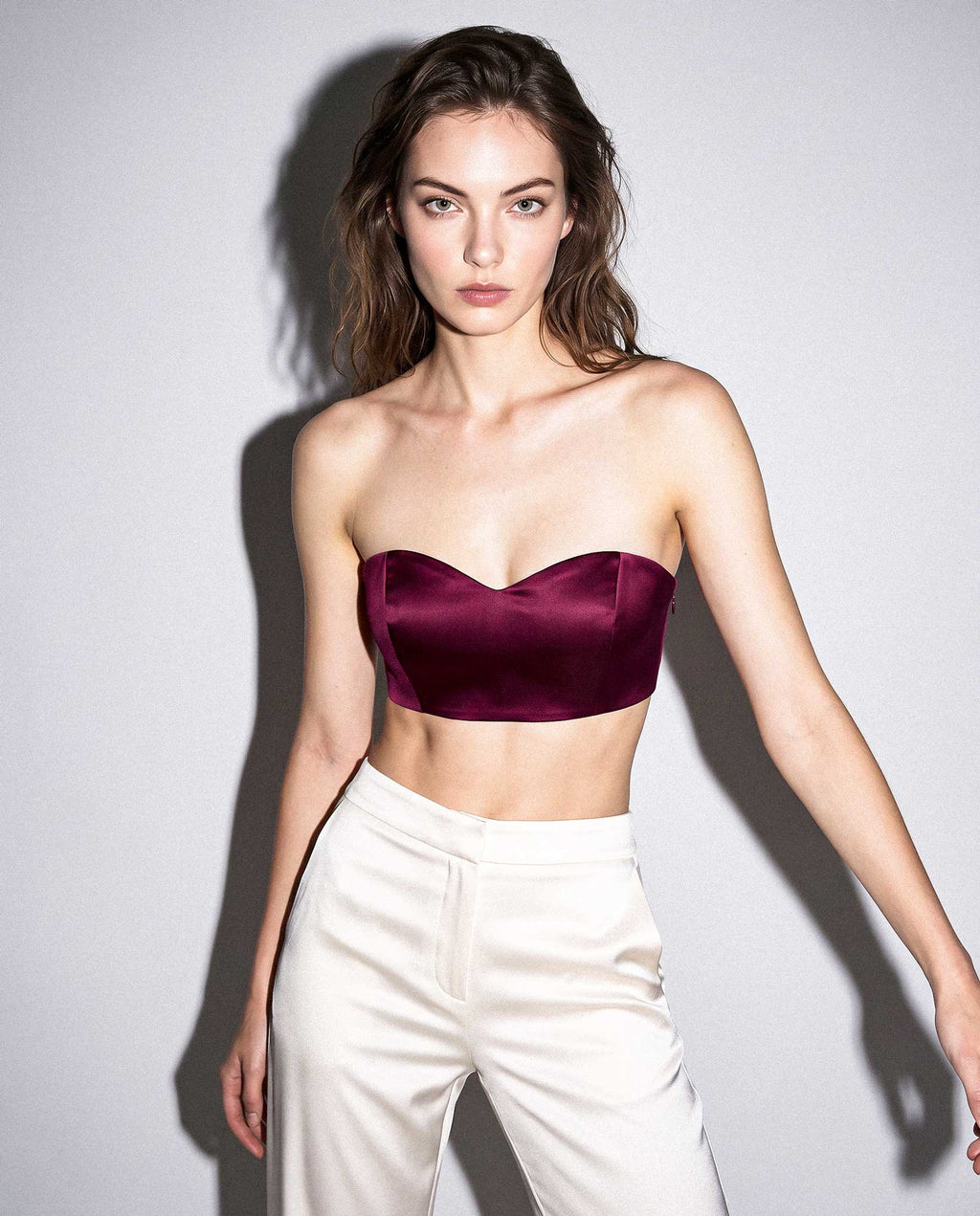 Model wearing a burgundy silk satin bandeau top with ivory trousers in a directional studio portrait